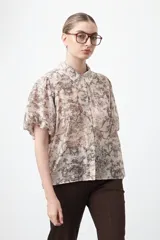 Camisa de manga corta abullonada, con cuello camisero y botones frontales. Presenta un estampado de inspiración barroca en tonos marrón y beige claro.