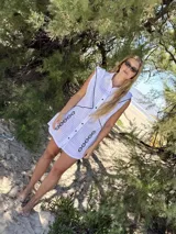 Vestido camisero corto blanco de algodón con bordados negros, cuello camisero, cierre frontal con botones y sin mangas.