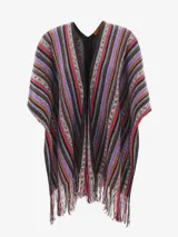 Capa o poncho de tejido de punto con cuello en V y flecos en el borde inferior. Presenta un patrón de rayas verticales en zigzag con una rica paleta de colores que incluye tonos marrones, negros, rojos, naranjas y morados.