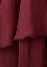 Vestido largo bordó con volantes en el cuello y mangas largas con volantes en los puños, diseño oversize y cierre de lazo delantero.