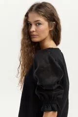 Blusa de lino negra, con escote redondo y mangas largas abullonadas con puños elásticos fruncidos.