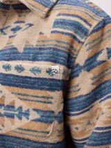 Camisa de manga larga con diseño de estampado étnico en tonos azules y beige. Presenta cuello clásico, cierre frontal con botones y bolsillos en el pecho.