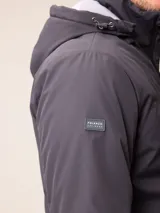 Campera de nylon gris con capucha, cierre frontal completo y bolsillos laterales. Presenta un diseño minimalista con logo bordado en el pecho.