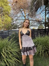 Vestido corto de tela metalizada en tono fucsia con reflejos dorados, con escote en V, diseño de top con triángulos, aberturas laterales en la cintura y doble volado irregular en el ruedo.