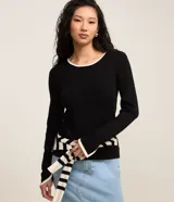 Sueter de punto color negro con cuello redondo, manga larga y detalles de vies contrastantes en color blanco en cuello y puños.