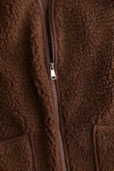 Chaleco de sherpa suave color marrón, con cierre frontal, ribetes de cinta finos y dos bolsillos de parche en la parte delantera. Forrado.