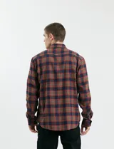 Camisa de franela a cuadros con cuello button-down, manga larga y botones de madera. Presenta dos bolsillos tipo parche en el frente con cierre de botón.