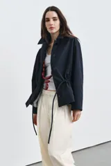 Parka de cuello alto con trabilla y manga larga, color azul marino. Presenta bolsillos laterales ocultos en la costura y cintura ajustable con cordón. El cierre frontal es con botones ocultos por solapa.