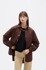 Campera marrón de manga larga confeccionada en algodón, con cuello camisero, cierre frontal con botones a presión y puños elásticos fruncidos.