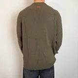 Sweater de tejido de punto grueso color verde militar, con cuello redondo y mangas largas tipo raglán. Presenta un corte holgado y una pequeña etiqueta con logo en el puño.