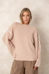 Buzo de punto acanalado vertical en color beige, con corte oversize, cuello alto y detalle de costuras decorativas en contraste a lo largo de los hombros y mangas.