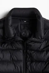 Chaleco negro acolchado con cuello alto y cierre frontal. Diseño sin mangas con bolsillos laterales con cierre y bolsillos interiores abiertos.