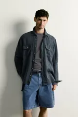 Camisa relaxed fit de lino color negro con efecto lavado, cuello clásico, manga larga con puños abotonados y dos bolsillos de parche con solapa en el pecho.