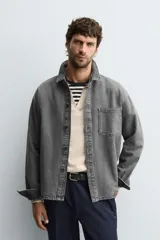 Camisa de denim de algodón, color gris oscuro lavado, de corte holgado (boxy fit). Presenta cuello solapa, manga larga con puño abotonado, bolsillo de plastrón en el pecho y cierre frontal con botones.