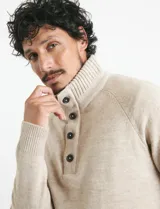 Sweater de punto color azul marino, con cuello alto, cierre frontal parcial y tapeta con botones. Presenta mangas raglán y puños y ruedo acanalados.