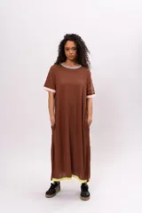 Vestido largo tipo remerón, color marrón con cuello redondo y mangas cortas con ribete rosa. Presenta ribete amarillo en el ruedo y bolsillos laterales.