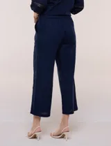 Pantalón crop de lino y algodón color blanco, con calce holgado, pierna ancha de corte recto y cintura elástica. Presenta bolsillos laterales y detalle de puntilla aplicada en el frente.