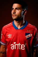 Camiseta de fútbol Umbro del Club Nacional de Football, modelo Away 2025 de color rojo con detalles en azul en el cuello en V y en las mangas. Cuenta con patrocinadores impresos en blanco, el logo de la marca y el escudo del club.