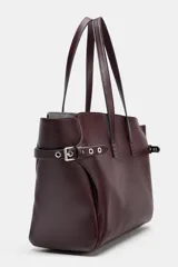 Bolso tipo shopper de gran tamaño en color bordó, con diseño estructurado y detalles de correas laterales con ojales metálicos y hebillas. Cuenta con doble asa de mano y cierre superior mediante imán.