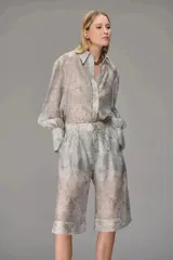 Camisa de organza con textura, de corte holgado, cuello clásico y mangas largas con puños abullonados. Presenta un diseño translúcido con estampado ornamental sutil.