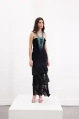 Vestido largo negro strapless de encaje con frunces en el torso, falda asimétrica en capas con volados y breteles removibles.