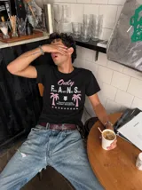Remera blanca de manga corta, con cuello redondo y diseño gráfico estampado en el pecho que incluye texto y palmeras.