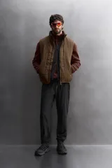 Chaleco marrón acolchado con cuello alto, cierre frontal con cremallera, bolsillos laterales con cremallera y bajo ajustable con trabilla y cremallera lateral.