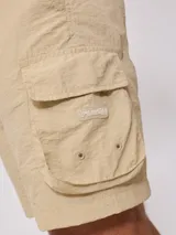 Bermuda cargo Rusty de corte recto, confeccionada en poliamida con acabado texturizado. Presenta cintura elástica con cordón de ajuste, bolsillos laterales tipo cargo con solapa y bolsillos frontales.