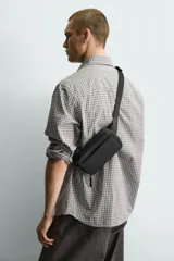 Riñonera negra con textura grabada, compartimento principal con cierre de cremallera y bolsillo frontal plano. Incluye asa ajustable con hebilla metálica de liberación rápida.