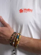 Remera blanca de algodón con estampado trasero en color naranja que incluye la palabra "Malibu", una hoja de palma y texto adicional.