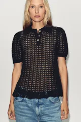 Polo negro de punto calado con cuello clásico, manga corta abullonada y terminación ondulada en el ruedo.