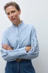 Camisa blanca de manga larga con cuello alto fruncido y bordados calados en el pecho y los hombros.