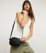 Cartera tipo camera bag marca Satinato de color negro, con forma ovalada, superficie texturizada, cierre superior con cremallera y correa ajustable.