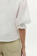 Blusa de lino blanca con escote redondo y mangas cortas abullonadas con detalles de volados en los puños.