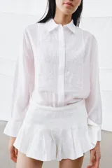 Camisa de corte fluido con cuello solapa y manga larga con puños. Presenta detalles de bordados a tono en el frente y cierre frontal con botones ocultos bajo solapa.