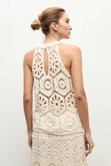 Top halter color beige claro, sin mangas, confeccionado en tejido de crochet con diseño de motivos geométricos y florales calados.