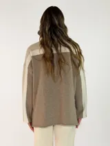 Sweater de punto con diseño color block en tonos gris oscuro, negro y gris claro. Presenta cuello alto, mangas largas y un corte holgado.