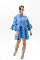 Vestido corto azul, estilo camisero, con cuello camisero, cierre frontal con botones y mangas acampanadas con volados. Presenta un diseño holgado con cortes fruncidos en el cuerpo.