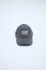 Gorra gris con visera curva, bordado frontal con texto en color beige y detalle bordado lateral.