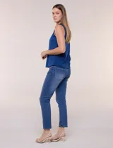 Chaleco blanco sin mangas de estilo smart-casual, con escote en V y costuras verticales de entalle. Cuenta con bolsillos o solapas simuladas a los lados de la cintura decorados con un botón metálico dorado y un largo a la cadera.
