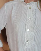 Blusa de manga larga con estampado de rayas verticales finas en tono beige. Presenta cuello redondo con volados, cierre frontal parcial con botones y puños con volados.