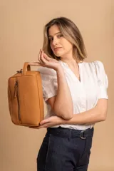 Neceser unisex de símil cuero color camel, con forma rectangular y asa lateral. Presenta un bolsillo frontal con cierre vertical y un compartimento principal con cierre superior.
