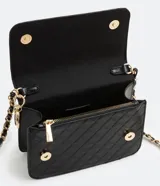 Bolso pequeño estructurado color negro, con textura capitoneada, asa de cadena y solapa frontal con botón a presión. Incluye divisor interno con cremallera.