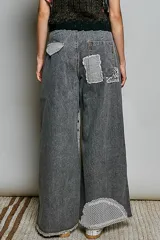 Pantalón de jean gris oscuro con corte holgado, parches asimétricos estilo patchwork con estampados de rayas y animal print en las rodillas, y detalle de tira central con botones a presión y encaje.