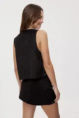 Chaleco de efecto gamuzado color negro, abierto con escote en V, detalles de tachas metálicas en los bordes y cordones entrelazados en los laterales.