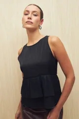 Top sin mangas de color negro con acabado metalizado sutil. Presenta un diseño con doble volado en la cintura que aporta movimiento y una caída liviana.