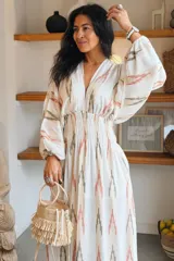 Vestido largo blanco con estampado geométrico en tonos rosa y gris, escote en V profundo, mangas abullonadas largas y cintura fruncida elastizada.