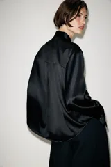 Camisa de satén color blanco, de corte clásico con cuello solapa, manga larga con puños y cierre frontal con botones dorados.