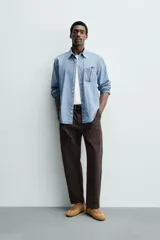 Camisa de corte regular fit confeccionada en tejido chambray de algodón con efecto lavado. Presenta cuello con botones, manga larga con puños abotonados, bolsillo en el pecho y cierre frontal de botones.