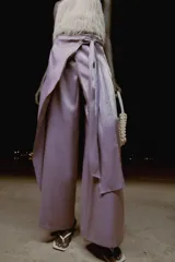 Pantalón de tiro alto con diseño cruzado tipo pareo, pernera ancha y detalle de lazada lateral. Presenta un acabado con efecto brillante.